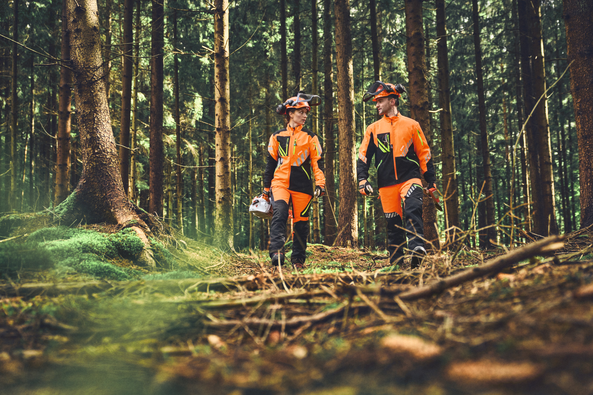 Deux personnes marchant dans la forêt, portant une veste STIHL ADVANCE FlexTEC et un pantalon de sécurité.