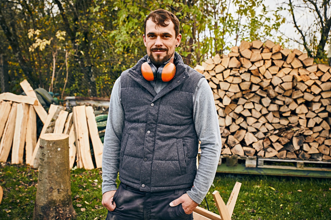 A man wearing STIHL ear protection in a garden, in front of stacked pieces of wood