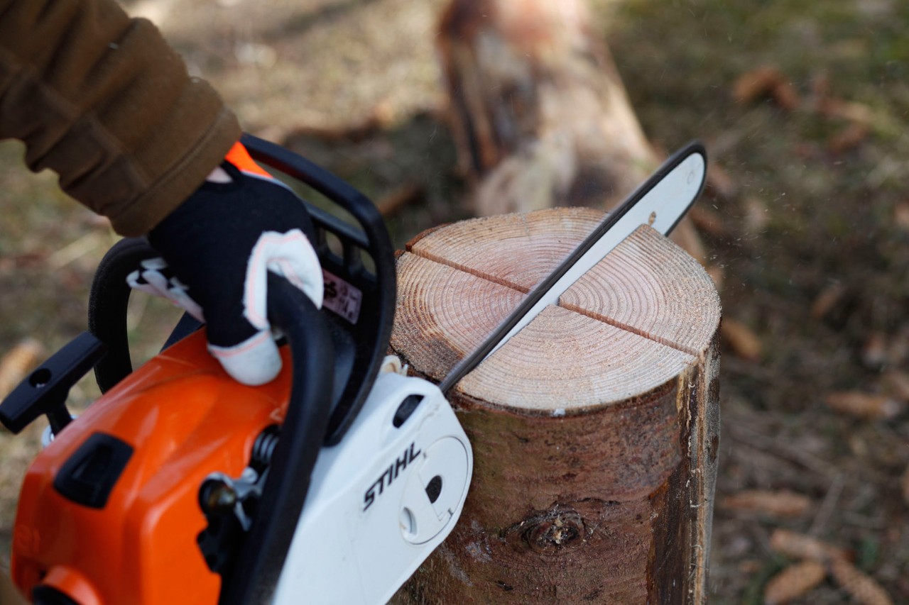 A STIHL MS 181 C petrol chainsaw being used to make two cuts into the end of an upright log, in a cross shape