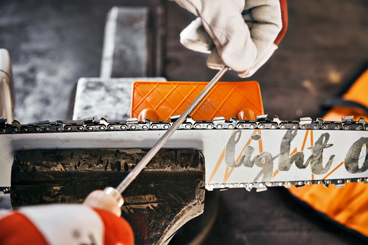 A person sharpening a STIHL chainsaw using a round saw chain file and a STIHL file angle plate