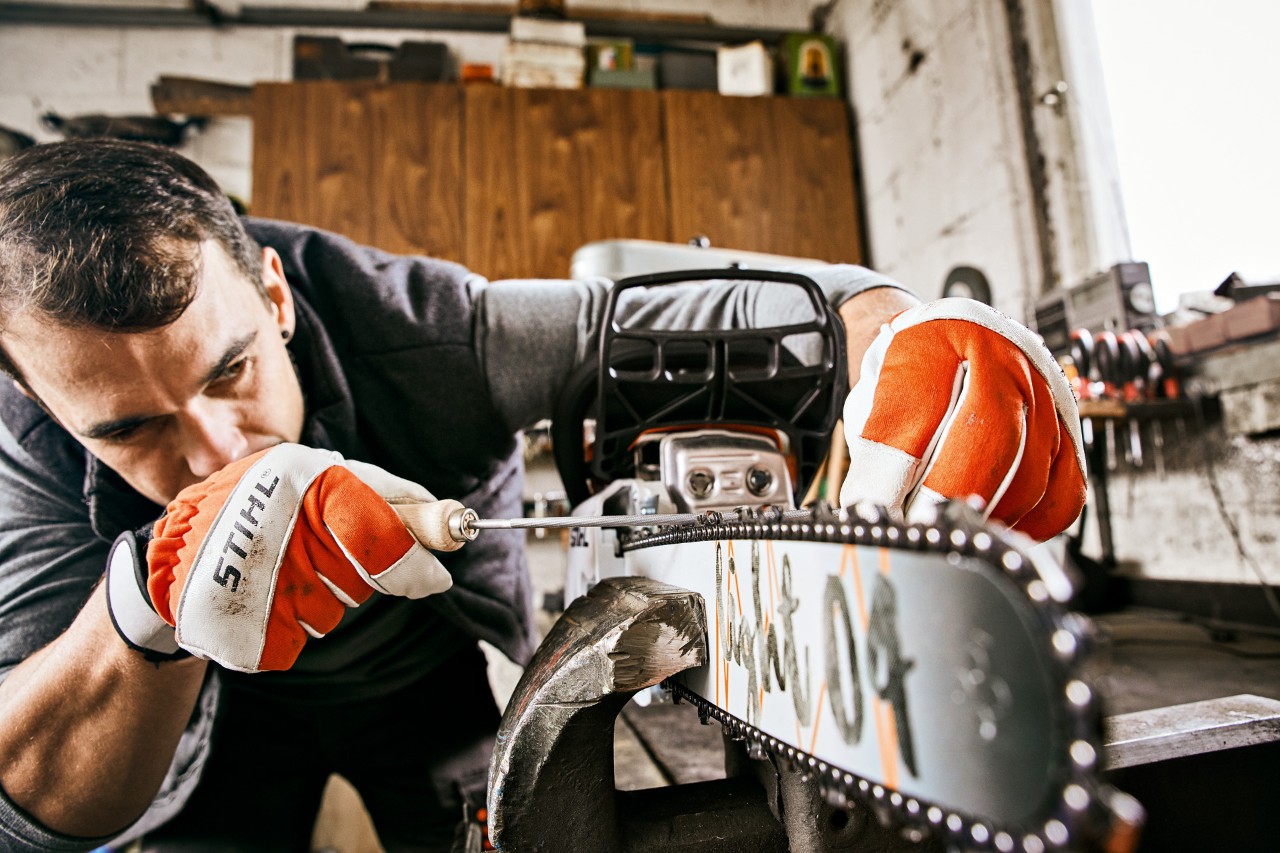 A man wearing STIHL gloves filing the chain of a STIHL 261 C-M petrol chainsaw with a round saw chain file