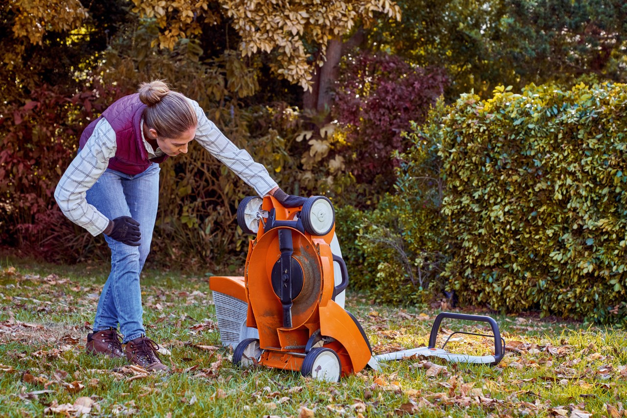 Une femme contrôle le dessous d’une tondeuse STIHL RMA 339 C dans le cadre de l’entretien de son gazon en automne