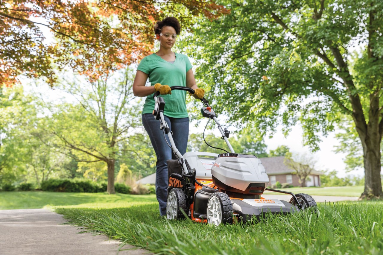 Un homme tond une pelouse à l’herbe haute avec une tondeuse à batterie STIHL RMA 448 TC, dans un jardin