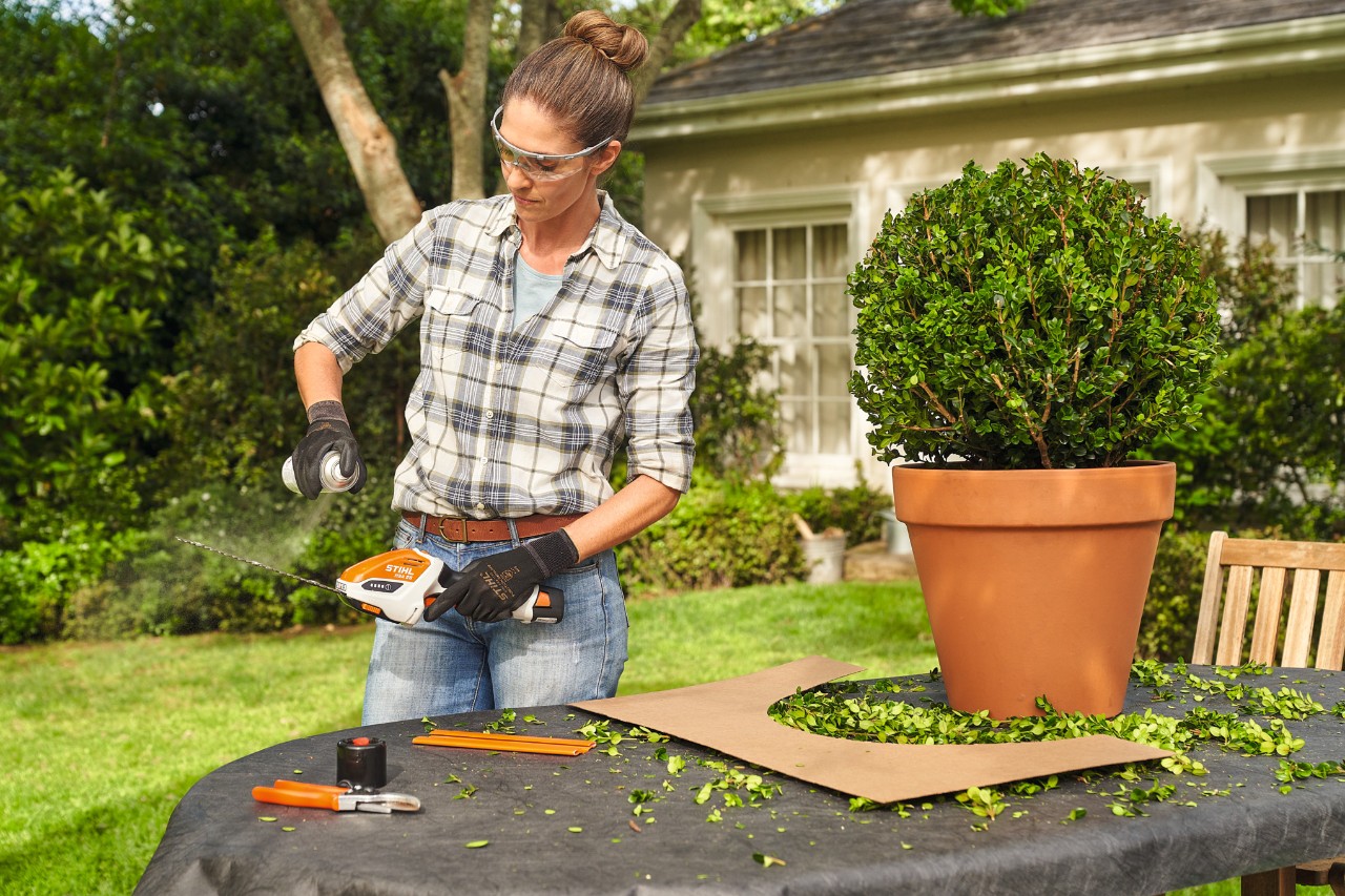 Une femme pulvérise du lubrifiant STIHL Superclean sur le taille-buis sur batterie STIHL HSA&nbsp;26 afin de le nettoyer après la taille