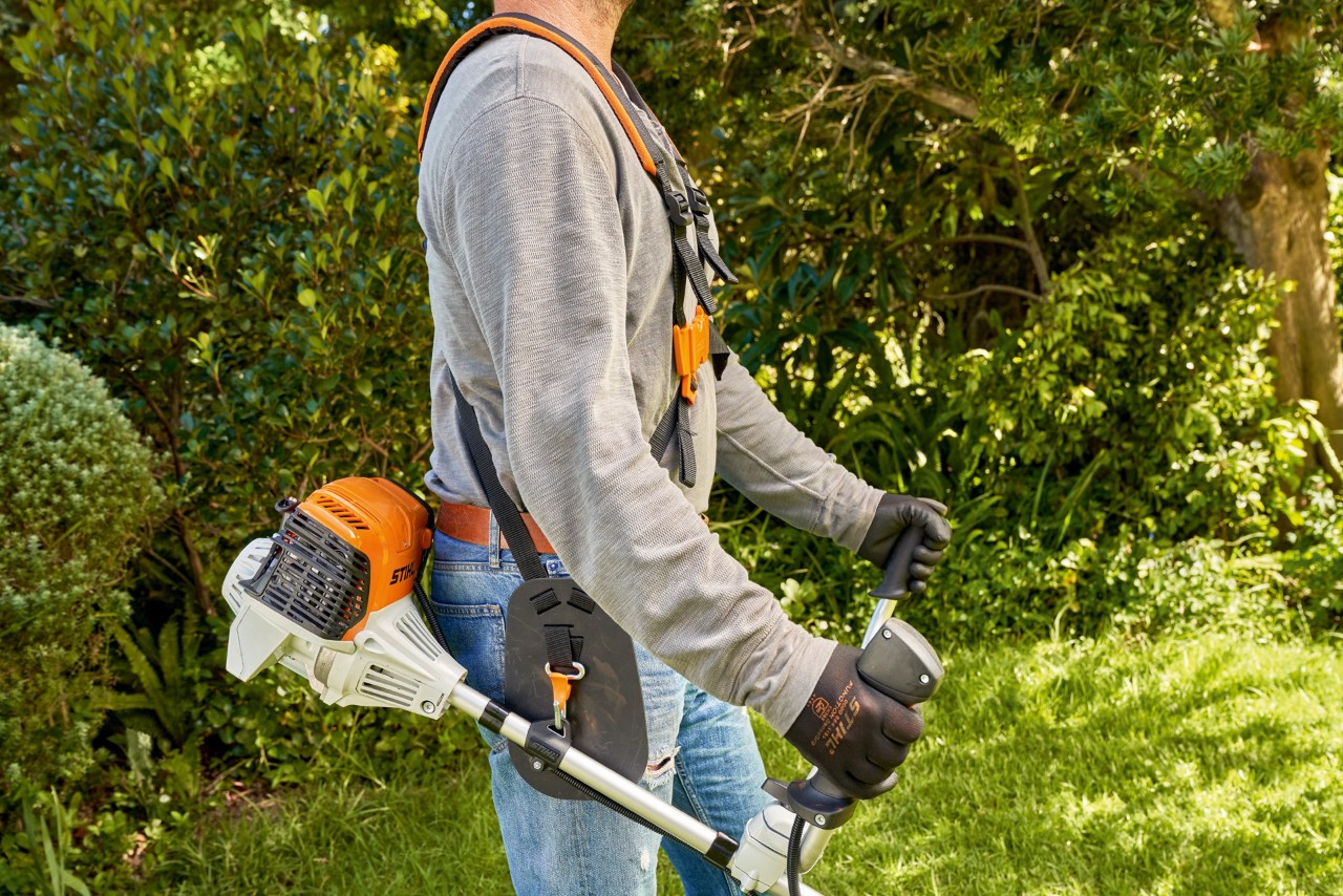 Un homme soulevant la débroussailleuse à essence STIHL&nbsp;FS&nbsp;91 du sol pour commencer la tonte 