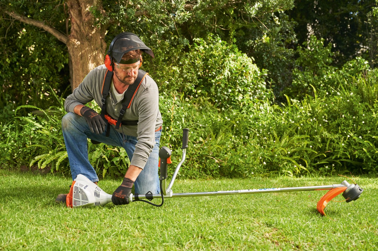 Un homme posant la débroussailleuse à essence STIHL&nbsp;FS&nbsp;56 au sol pour la démarrer