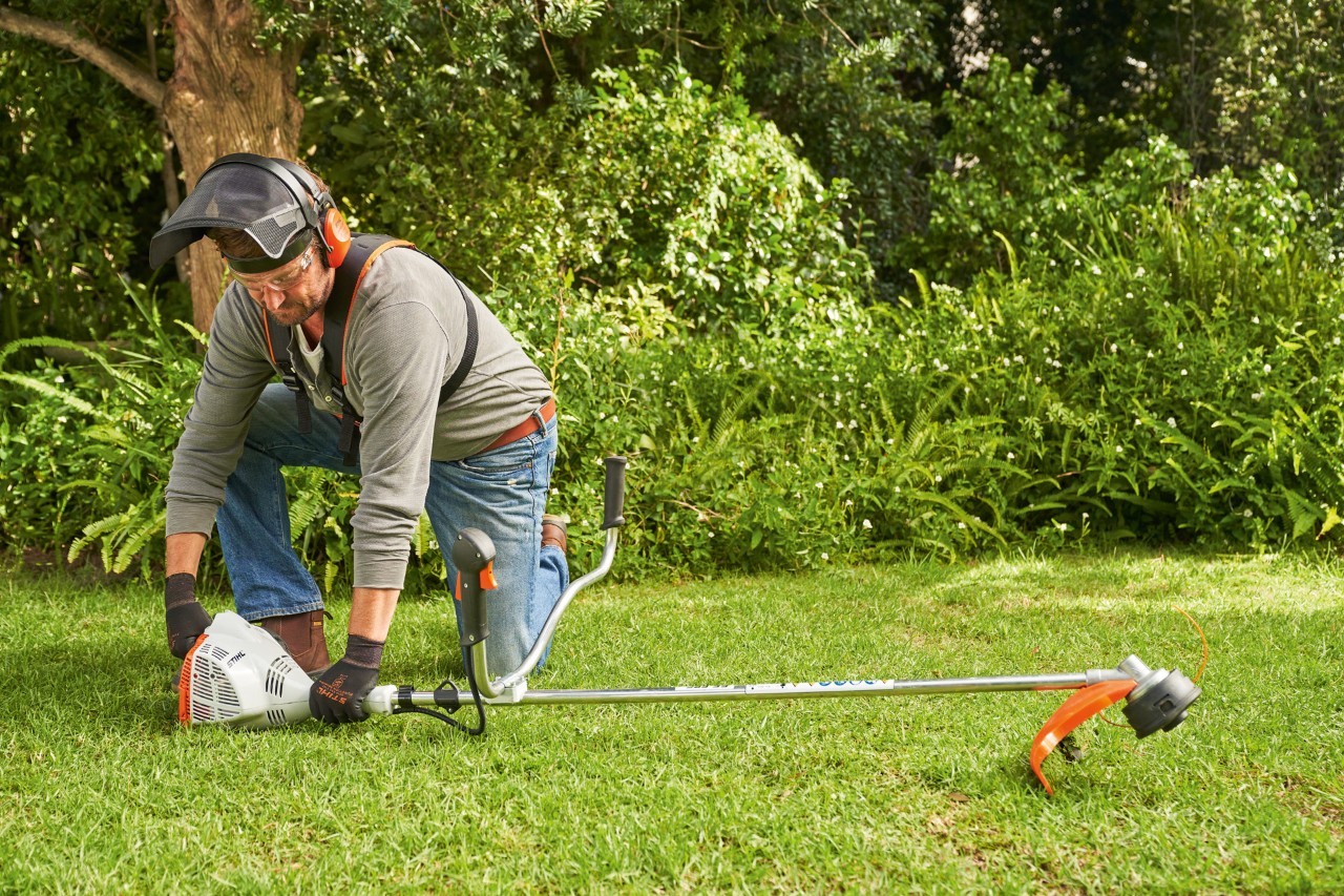Un homme maintenant la débroussailleuse à essence STIHL&nbsp;FS&nbsp;56 au sol pour la démarrer