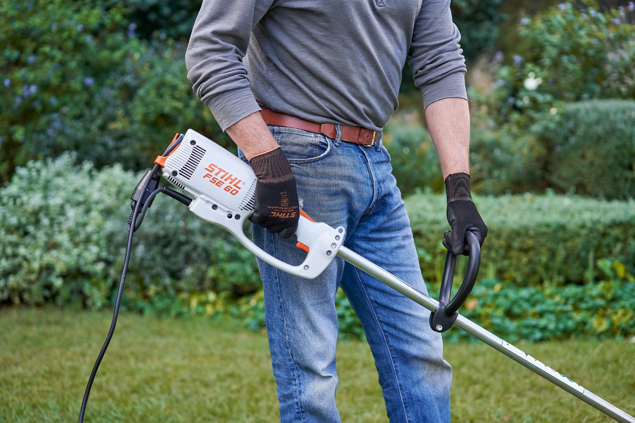 Un homme portant des gants de protection et tenant la débrousailleuse électrique STIHL&nbsp;FSE&nbsp;60 des deux mains