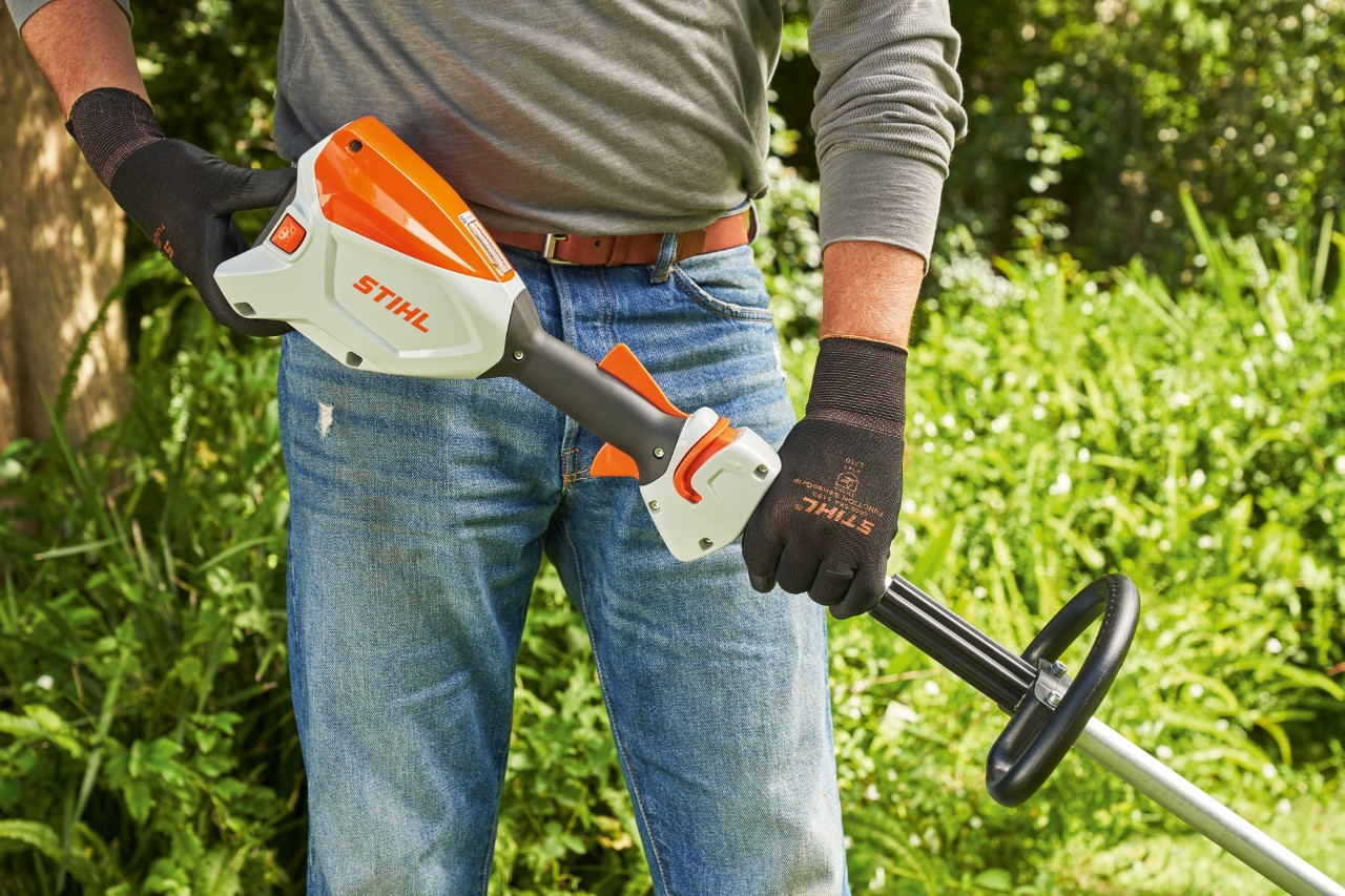Un homme portant des gants de protection et contrôlant la batterie de la débroussailleuse à batterie STIHL&nbsp;FSA&nbsp;60 pour pouvoir la démarrer