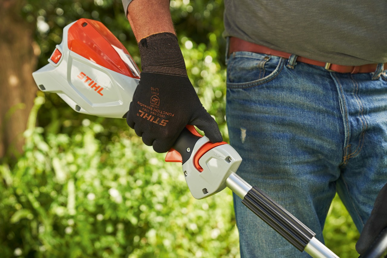 Un homme portant des gants de protection et poussant le dispositif de déverrouillage de la débroussailleuse à batterie STIHL&nbsp;FSA&nbsp;60 vers la poignée circulaire