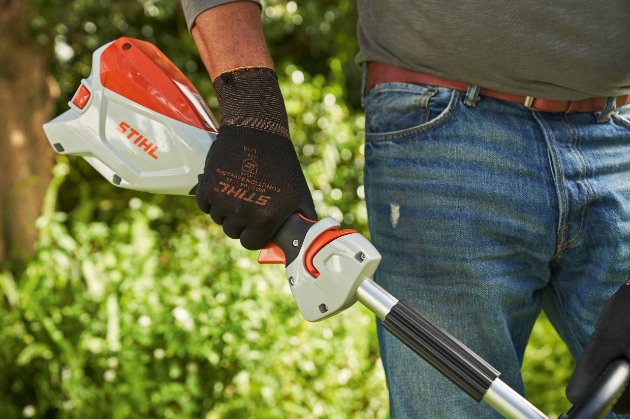 Un homme portant des gants de protection et appuyant sur le dispositif de blocage du levier de commande de la débroussailleuse à batterie STIHL&nbsp;FSA&nbsp;60 