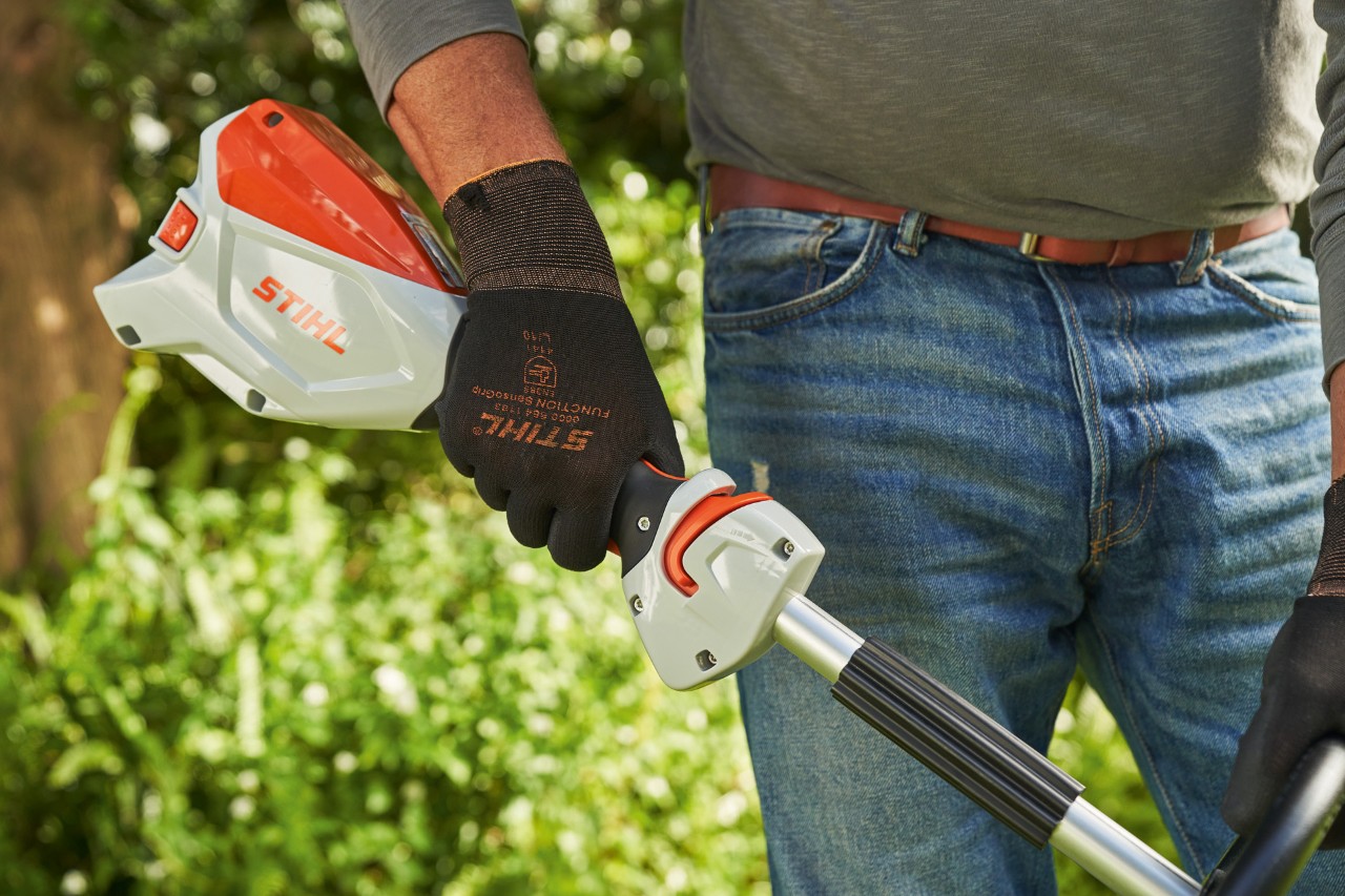 Un homme portant des gants de protection et appuyant sur le levier de commande de la débroussailleuse à batterie STIHL&nbsp;FSA&nbsp;60 afin de la démarrer