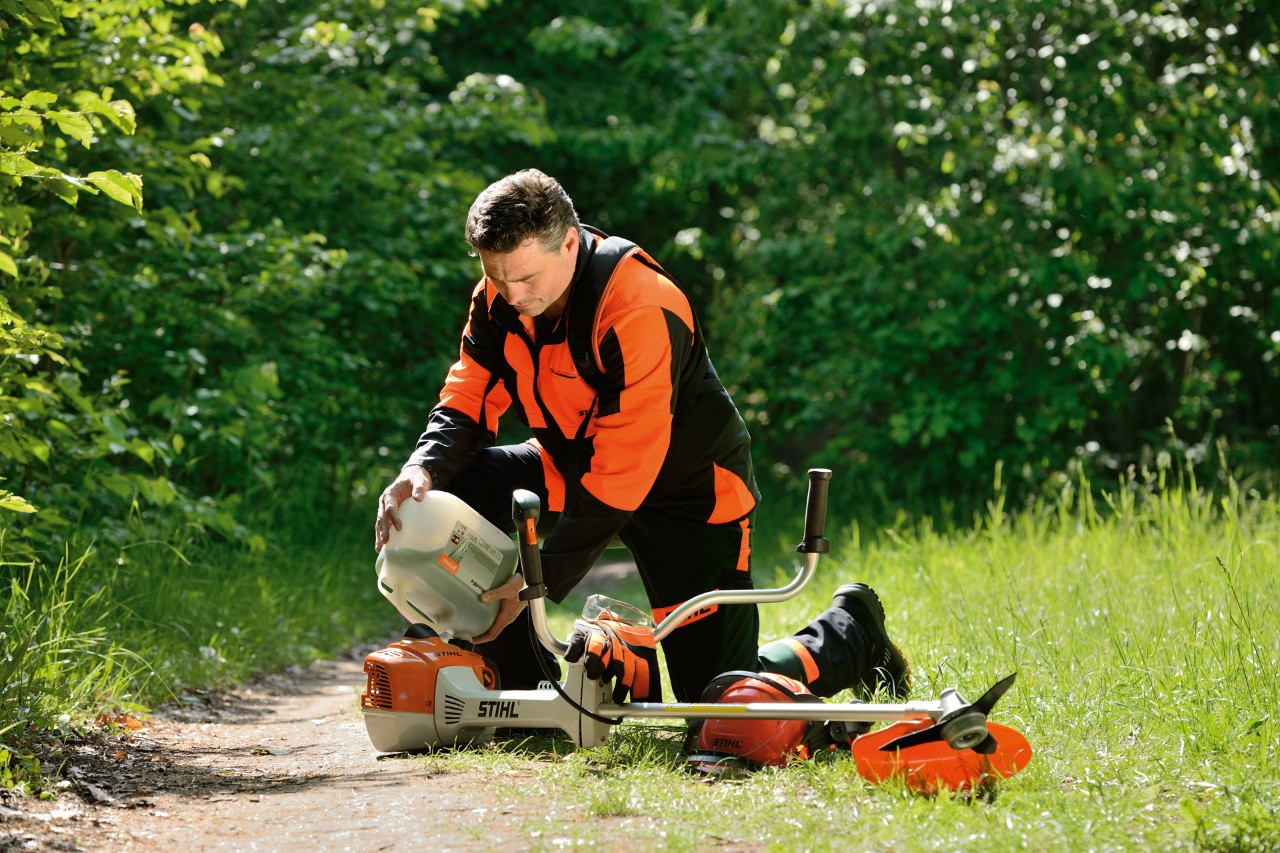 Un homme portant un équipement de protection STIHL et faisant le plein de sa débroussailleuse STIHL avec un mélange essence/huile