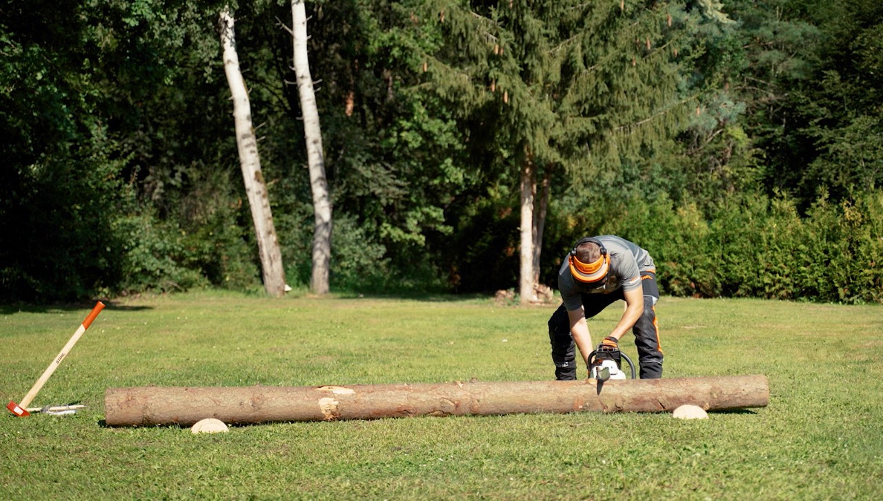 Une personne munie d’un équipement de protection commence à tronçonner un tronc d’arbre en bois de chauffage à l’aide d’une tronçonneuse STIHL