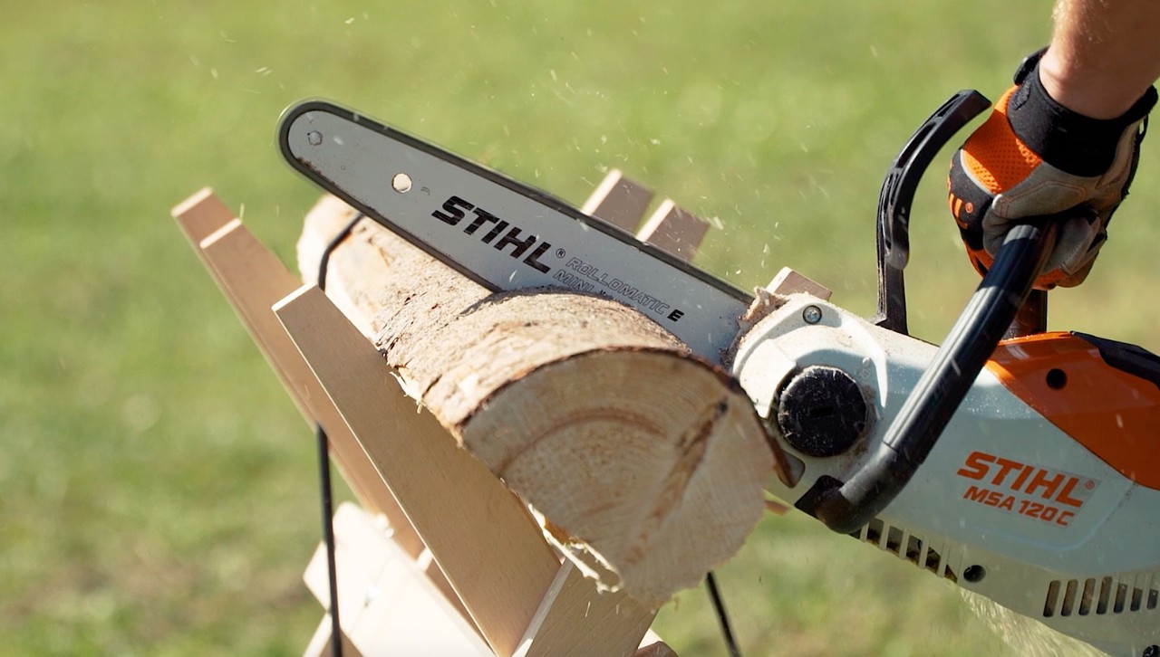 Une bûche sur un chevalet de sciage est coupée en bois de chauffage à l’aide d’une tronçonneuse STIHL MSA 120 C