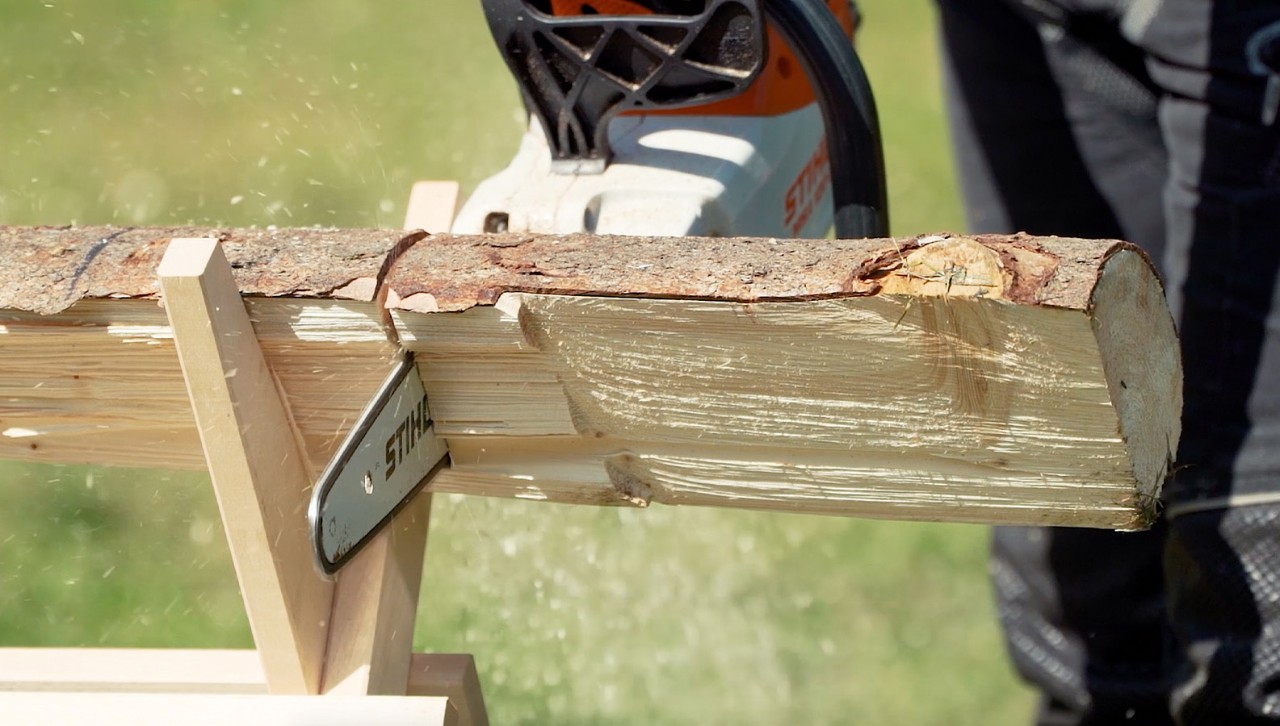 Une bûche sur un chevalet de sciage est coupée en bois de chauffage à l’aide d’une tronçonneuse STIHL MSA 120 C