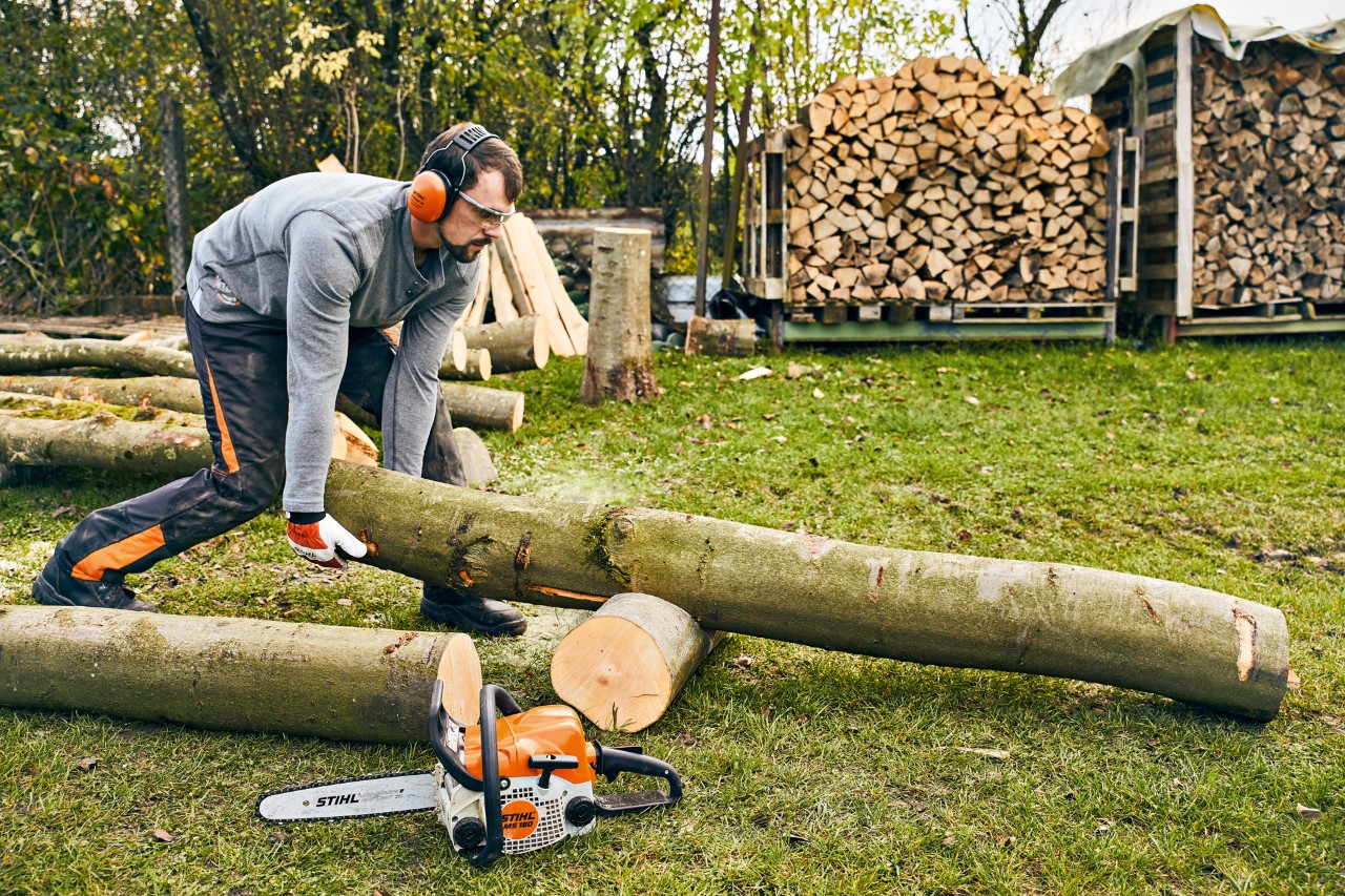 Un tronc d’arbre est repositionné sur un support de découpe, avec une tronçonneuse thermique STIHL MS 180 en premier plan.