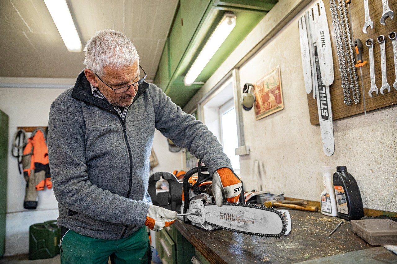Alt text: Un homme tend une chaîne de tronçonneuse STIHL dans un atelier
