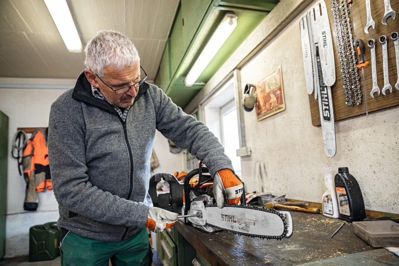 Homme dans un atelier vissant un élément sur une tronçonneuse dotée du guide-chaîne STIHL Rollomatic E 