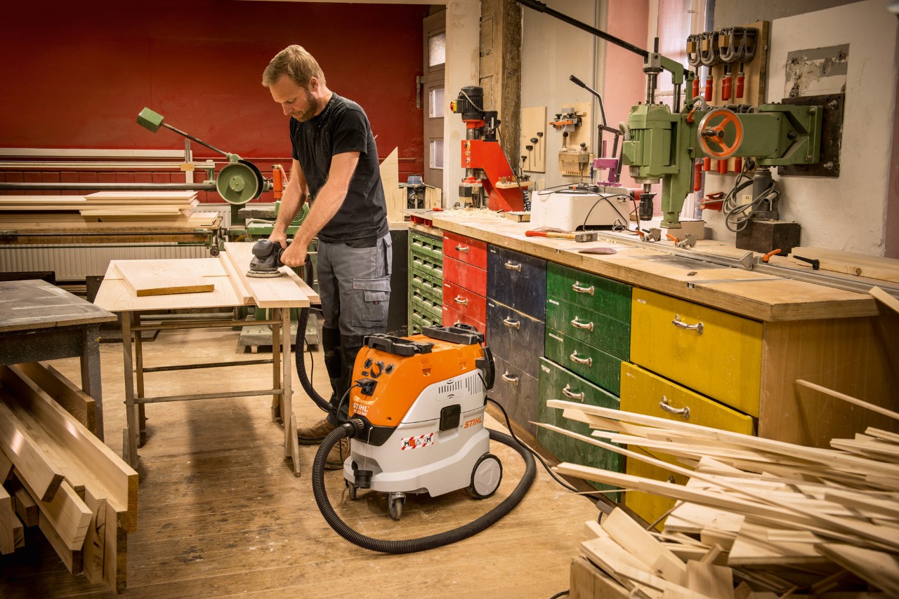 Homme travaillant avec des planches de bois dans un atelier et utilisant un aspirateur eau et poussière STIHL SE 133 ME