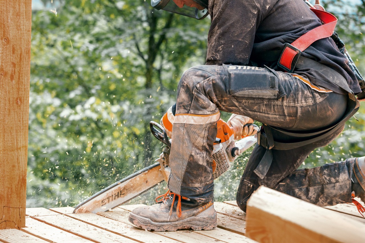 Personne portant des bottes de travail et un pantalon STIHL Advance X-Light sciant le bord d’une plateforme en bois.