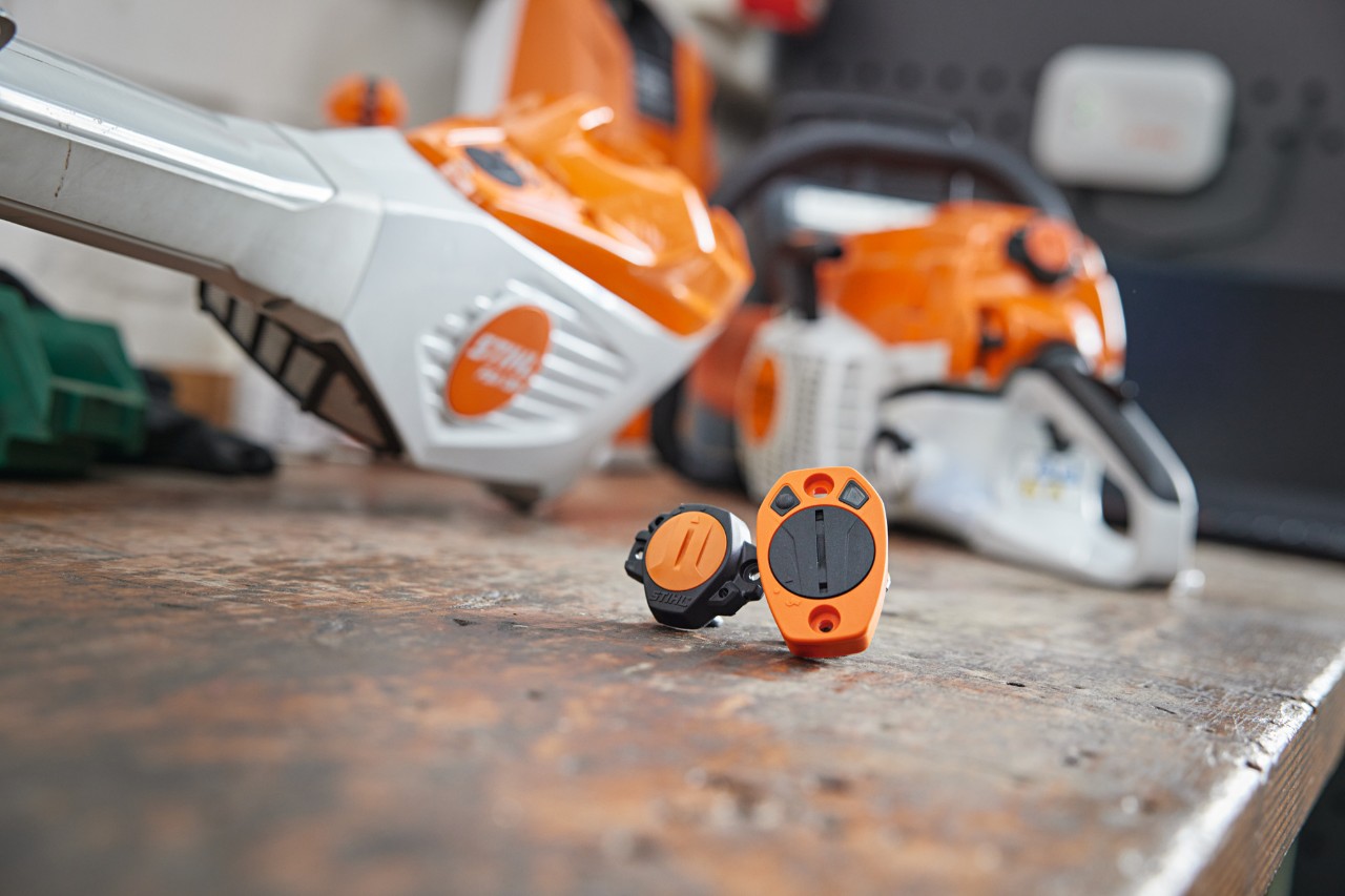 Un STIHL&nbsp;Smart&nbsp;Connector et un STIHL&nbsp;Smart&nbsp;Connector&nbsp;2&nbsp;A sont posés sur un établi. Différentes machines STIHL sont visibles en arrière-plan en flou.