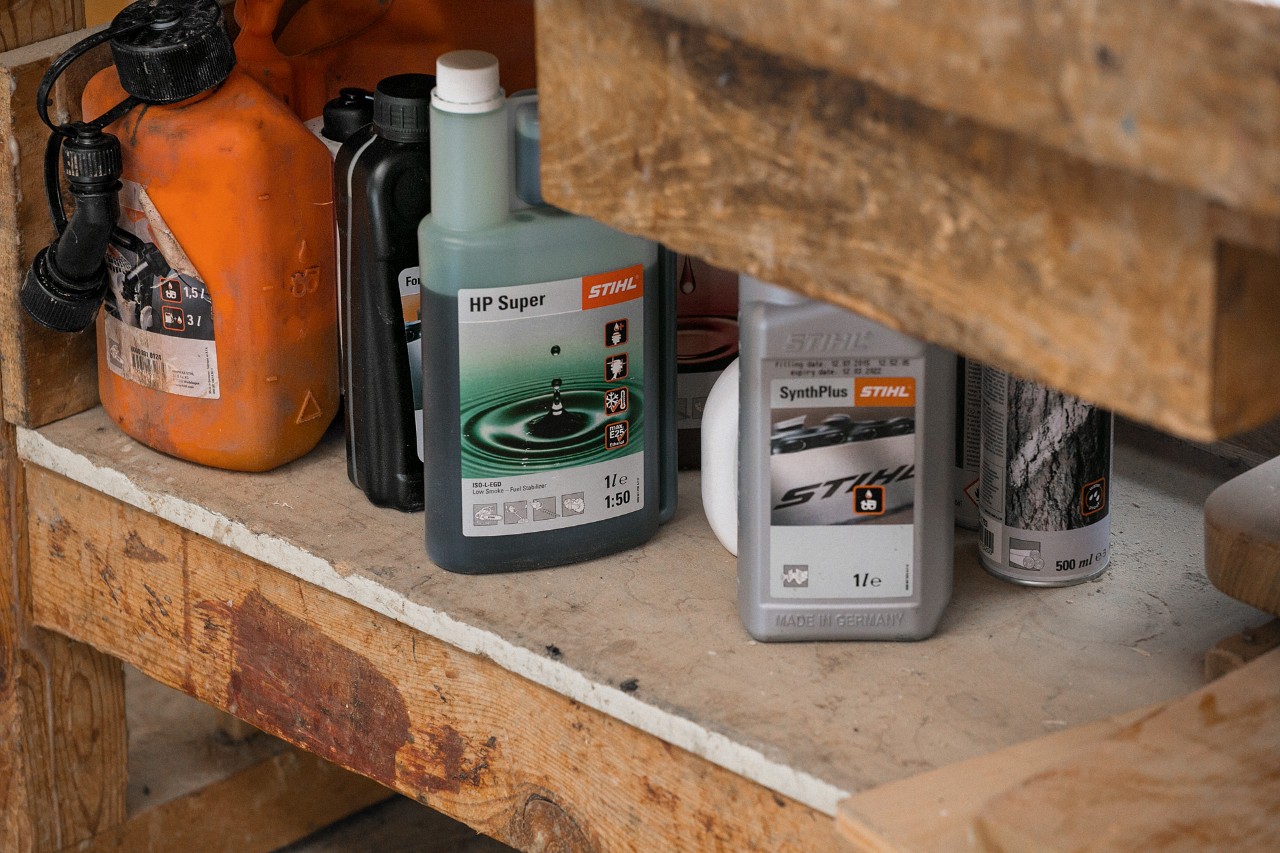 Huile adhérente pour chaîne de tronçonneuse STIHL SynthPlus et huile pour moteur deux temps STIHL HP Super à côté d’autres consommables sur une étagère