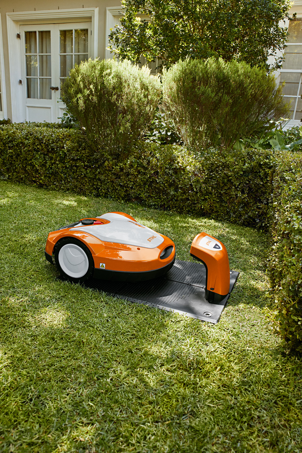 Une tondeuse robot STIHL iMOW® RMI 632 dans sa station de charge dans un jardin