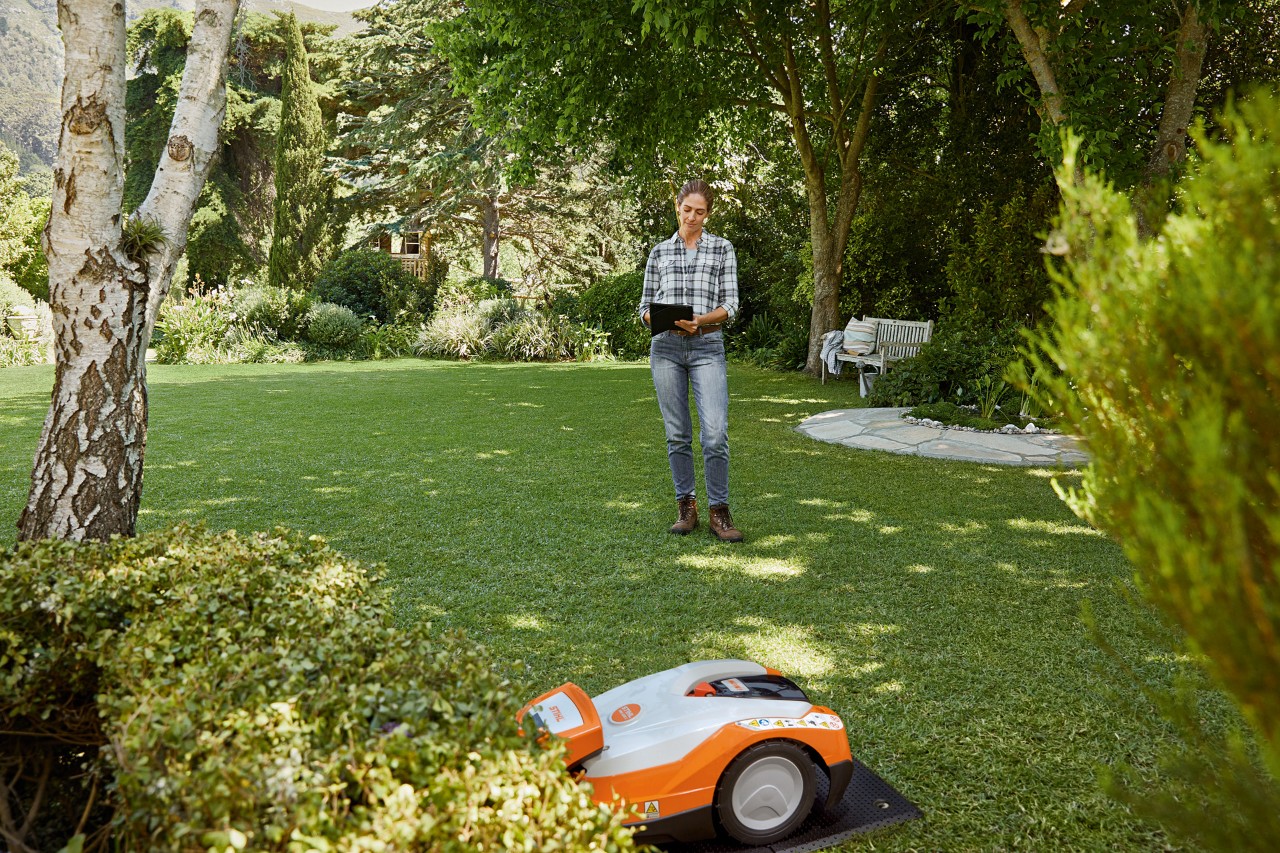 Femme avec une tablette dans un jardin utilisant un robot de tonte STIHL iMOW® 522