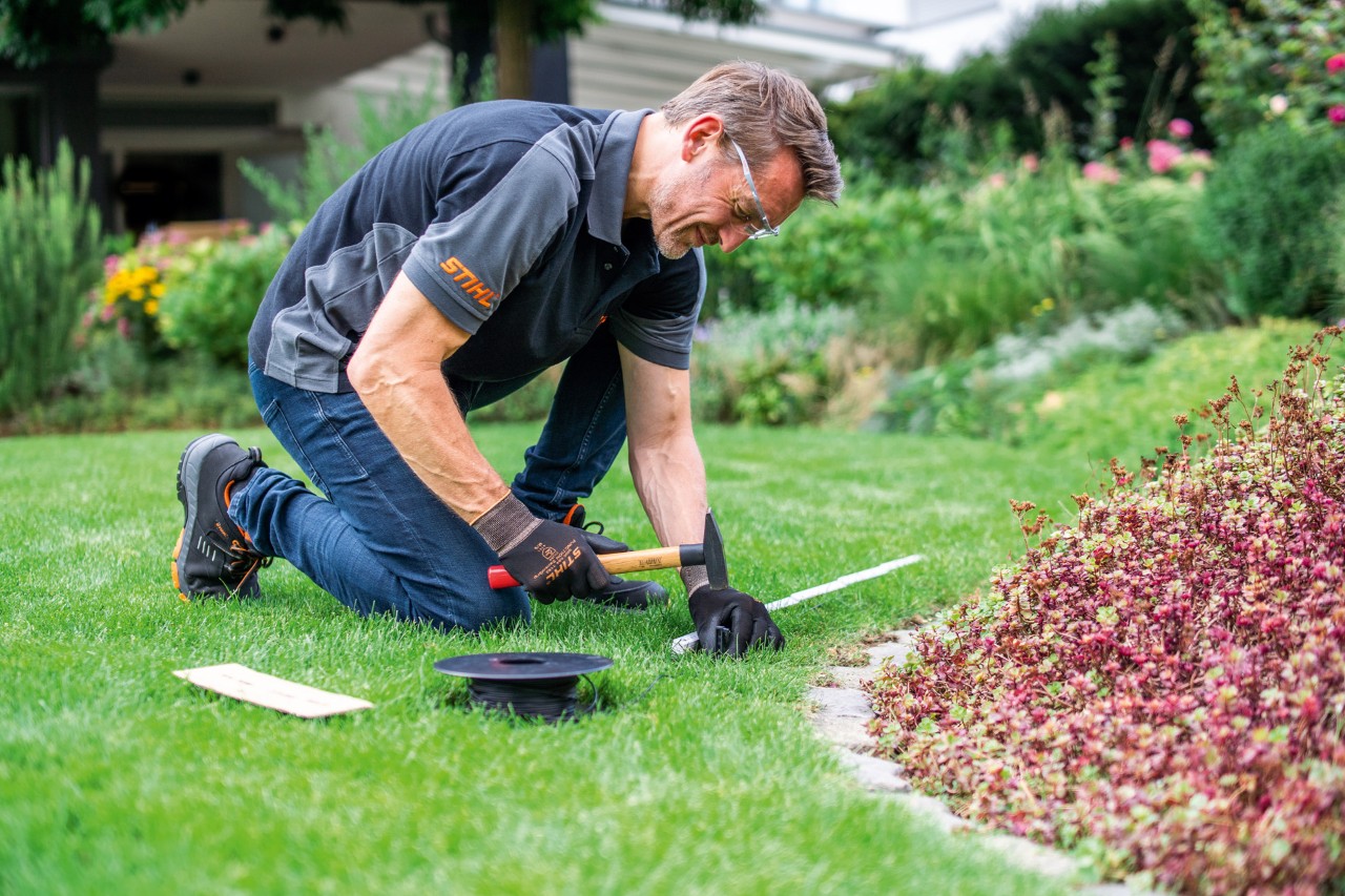 Un revendeur STIHL posant un fil de délimitation dans le jardin devant une plate-bande