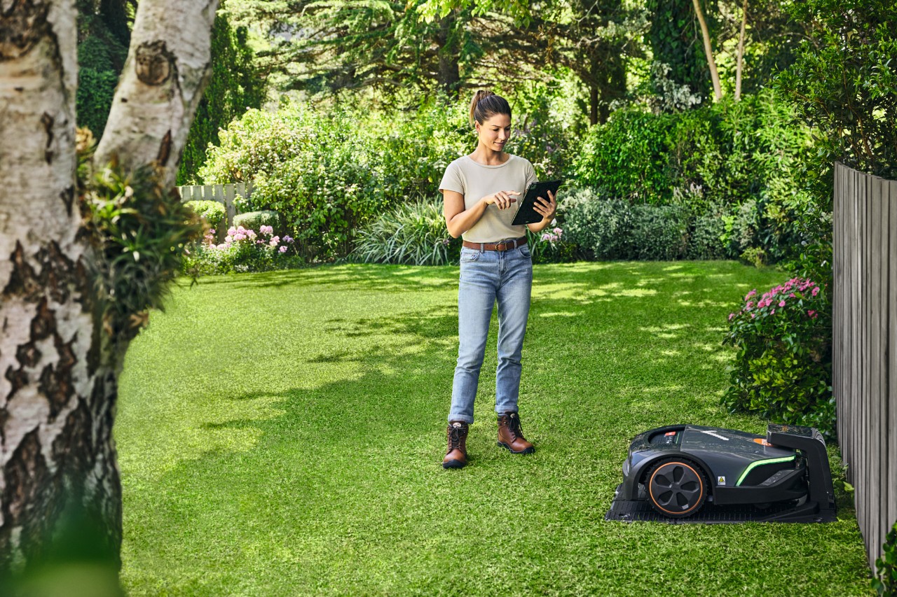 Une femme utilise la STIHL iMOW® EVO via une tablette dans son jardin